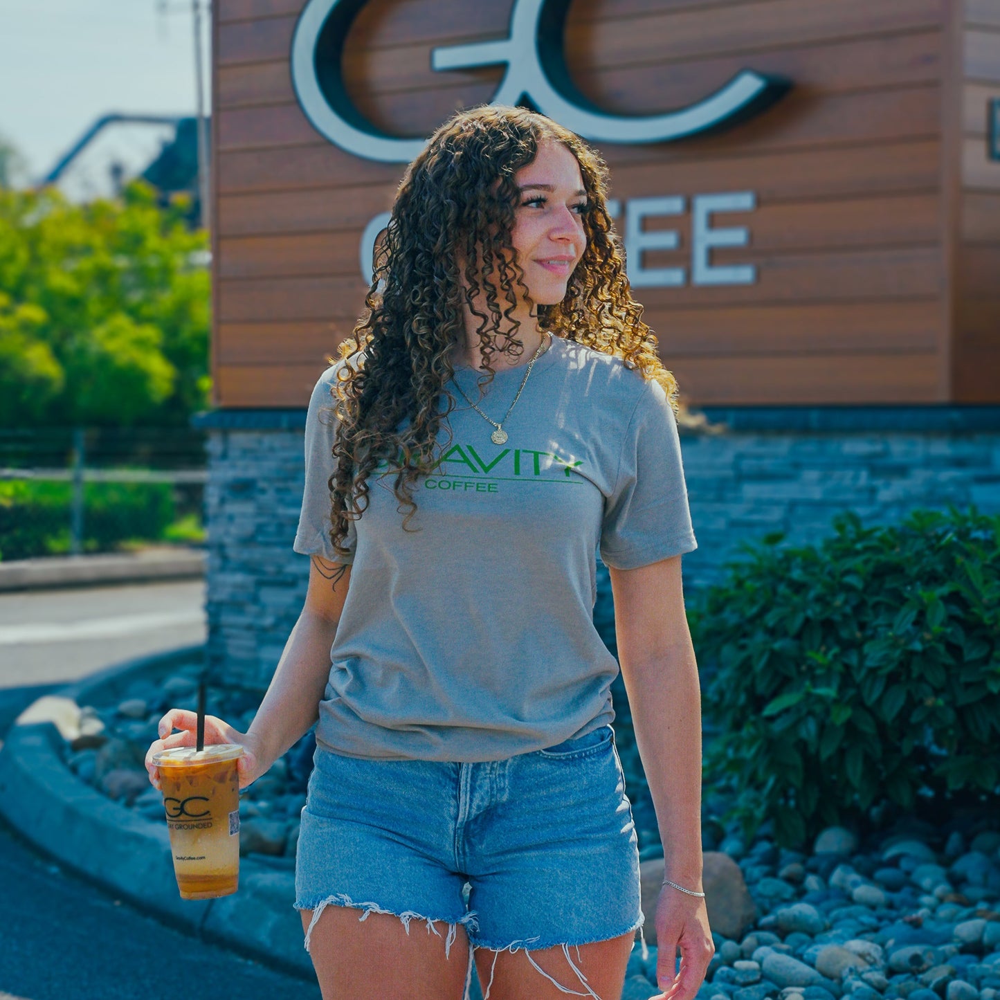 Woman holding a drink in front of a 'GC Coffee' sign