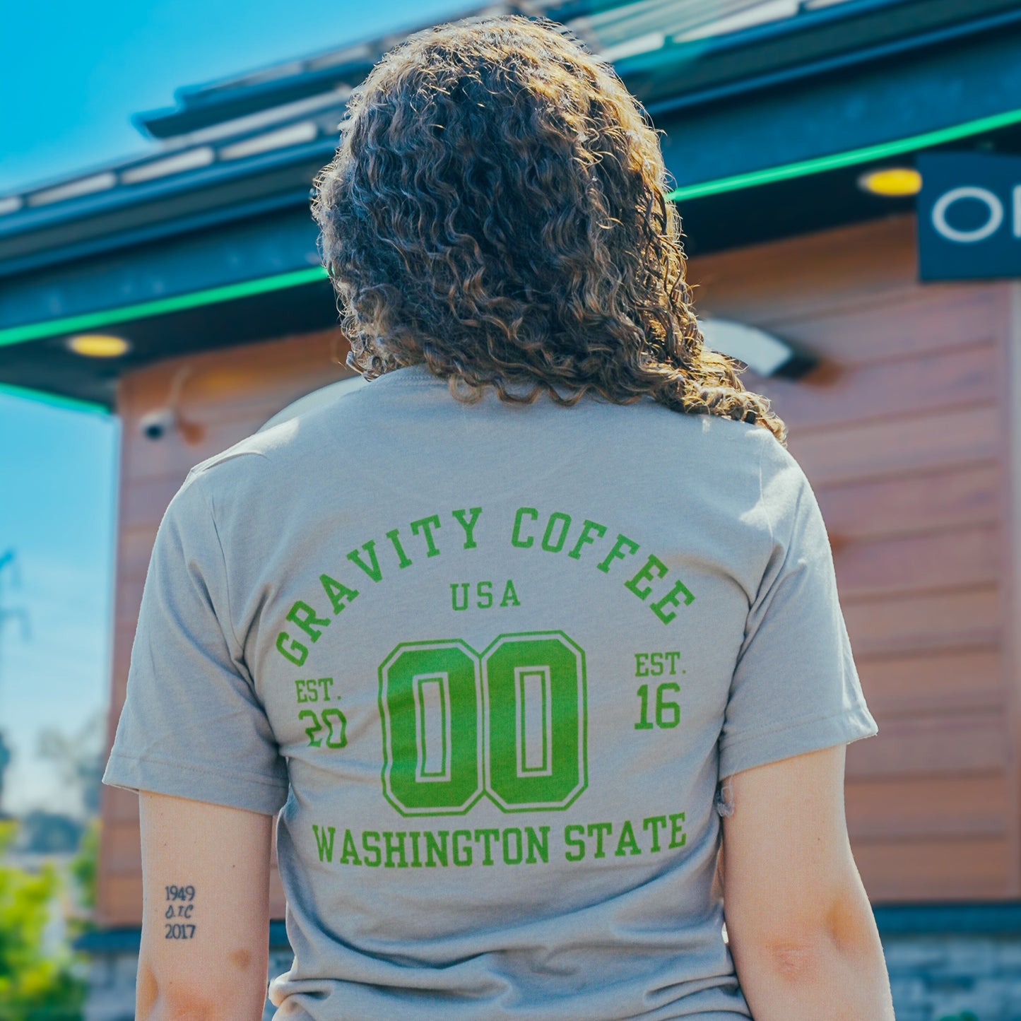 Person wearing a 'Gravity Coffee USA' t-shirt with 'Washington State' text outdoors.