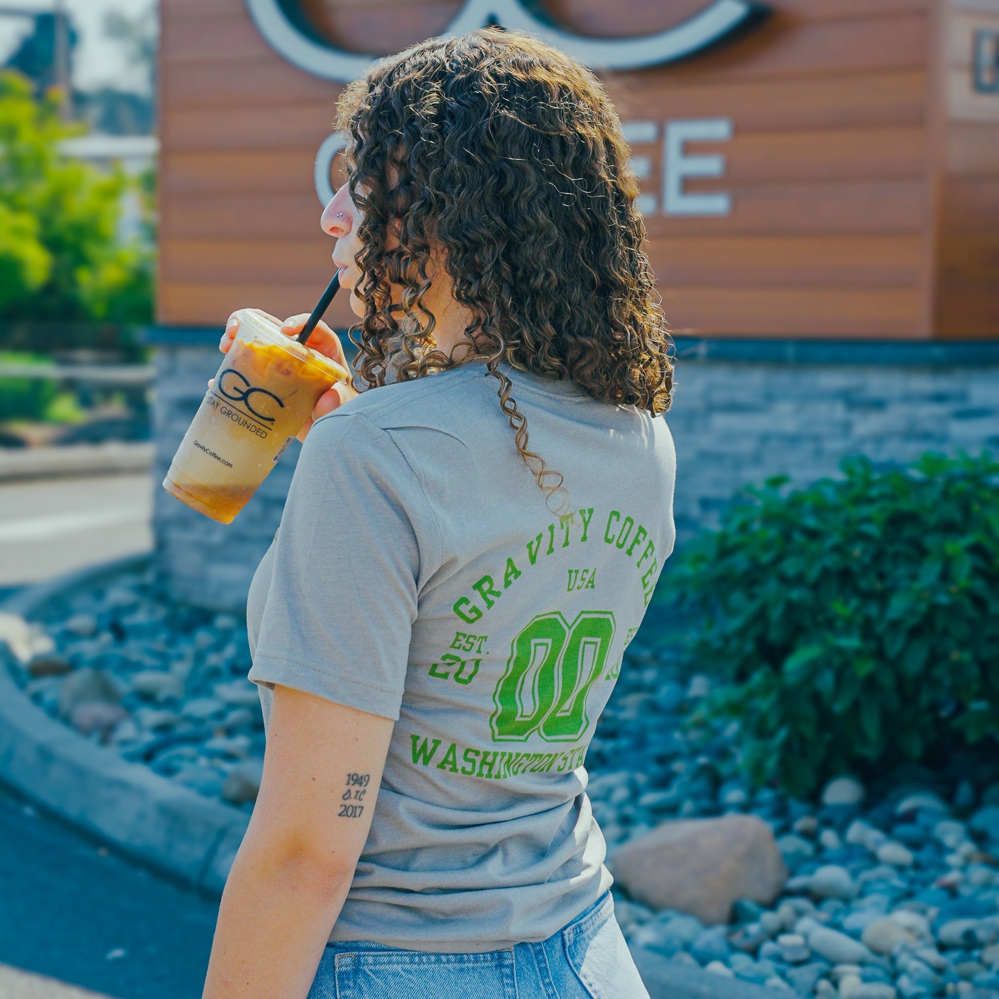 Woman drinking from a cup with a logo in front of a store with 'GC' branding.
